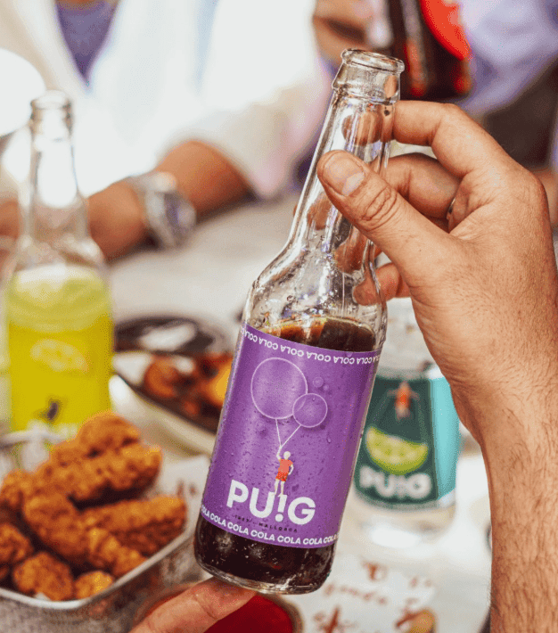 Mano sujetando refresco de cola, fondo de mesa con comida