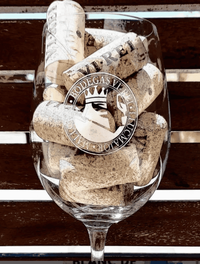 Copa amb el logotip de Bodegas Vi Rei gravat al vidre, plena de suros d'ampolles de vi del mateix celler.