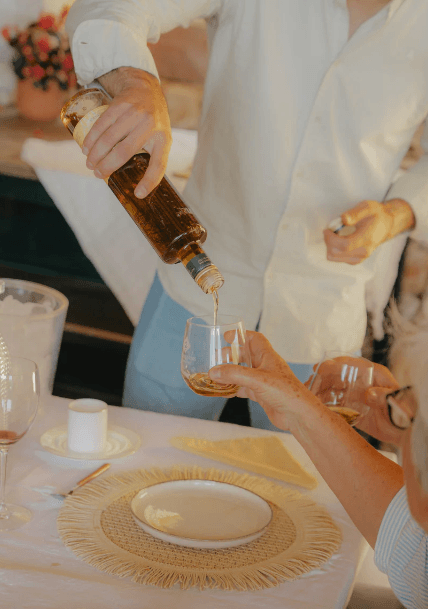 Image of an adult person serving Mallorcan herbal liqueur in a glass to another adult person