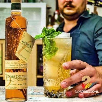 Imagen de cóctel elaborado con licor de hierbas Mallorquinas dulces, junto al cocktel se encuentra la botella de licor de hierbas mallorquinas dulces