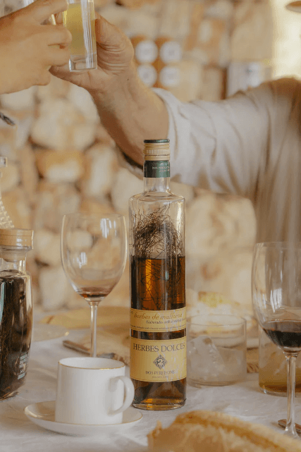 Imagen de una botella de licor hierbas mallorquinas dulces encima de una mesa donde han terminado de comer