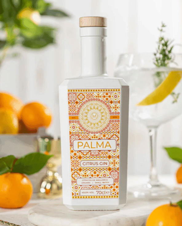 Imagen de botella citrus sobre mesa, en segundo plano se ve un frutero con frutas cítricas y un gin tonic